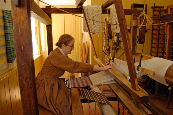 a woman demonstrates weaving on a floor loom at Black Creek Pioneer Village