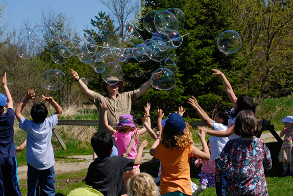 a man releases large bubbles into the air as children reach out to catch them